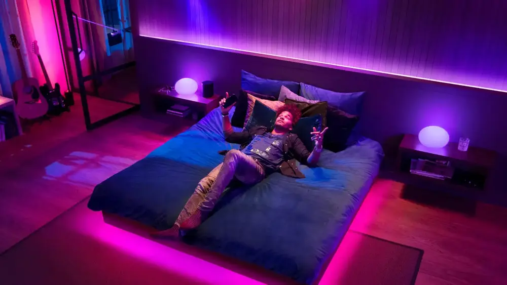 A person relaxing on a bed in a room illuminated by vibrant pink and purple LED lights, creating a cozy ambiance with modern decor.