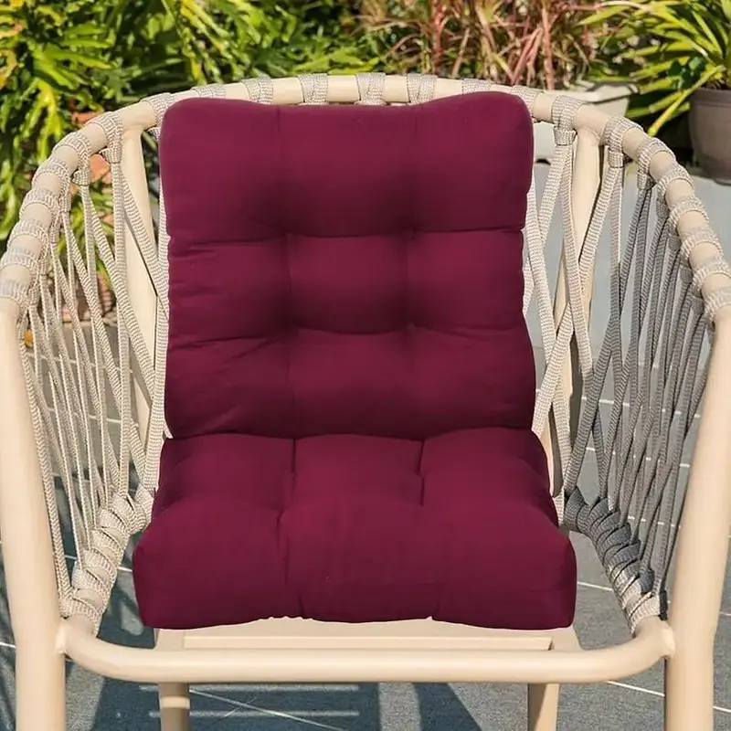 Burgundy cushion pad on a beige rope woven outdoor chair, surrounded by greenery.