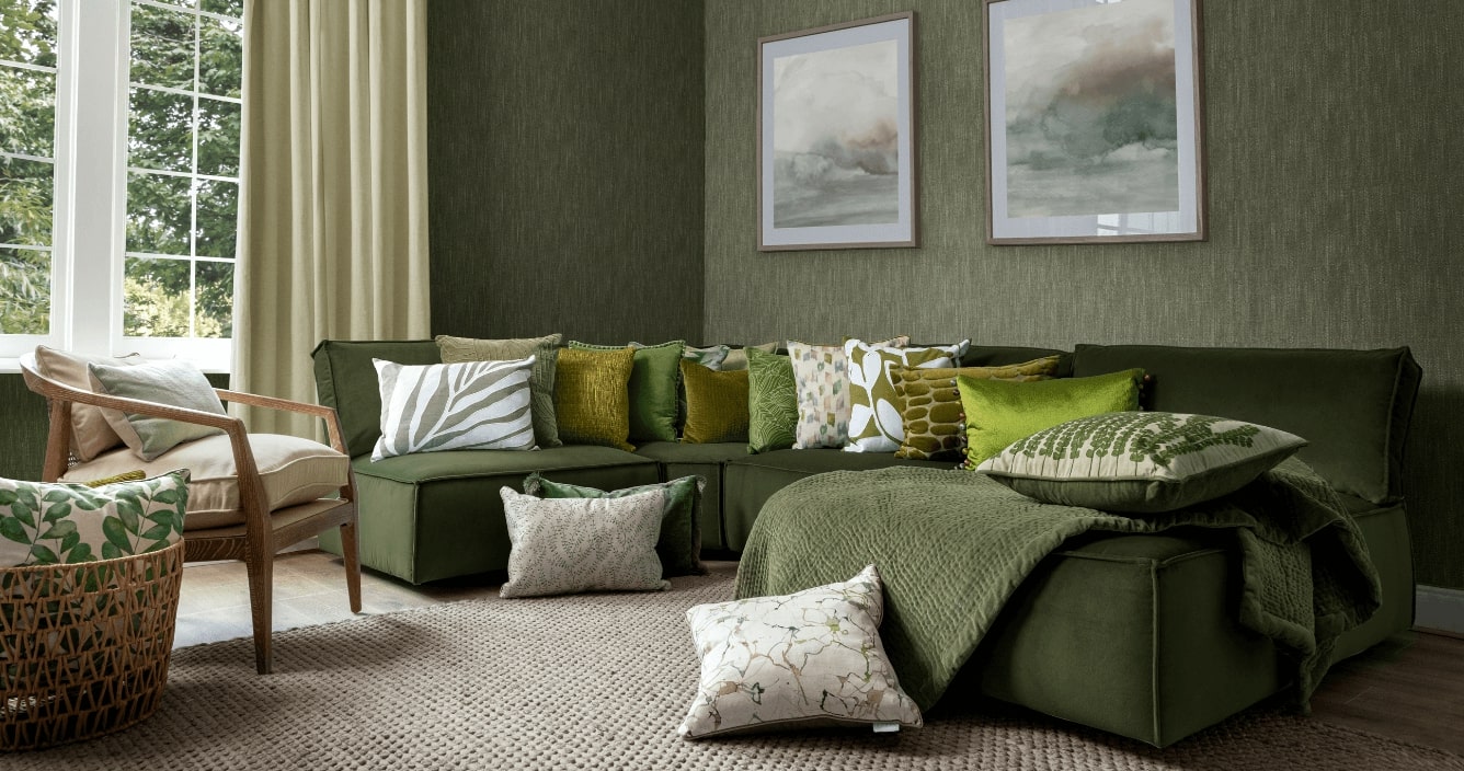 Stylish living room with a green sectional sofa, patterned throw pillows, and a beige armchair next to a window with curtains. Green textured wall with framed art adds to the cozy interior design.