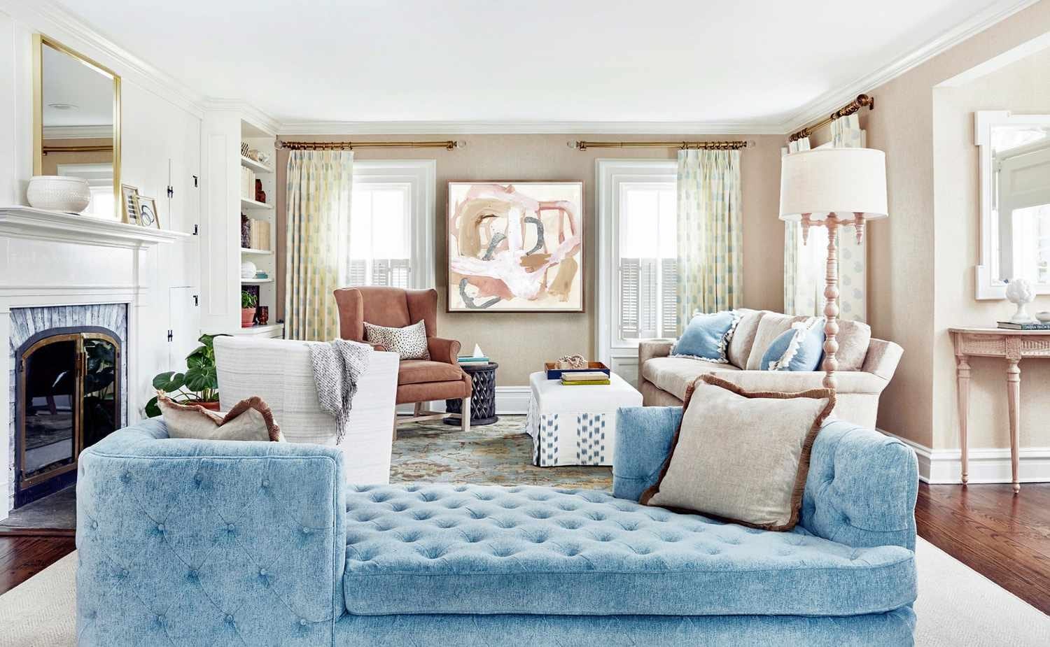 Elegant living room interior with a blue tufted sofa, armchairs, and neutral-toned decor, featuring a modern abstract painting above a fireplace.