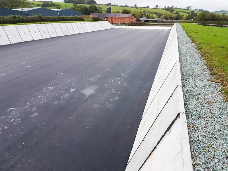 Silage clamp with concrete walls and asphalt flooring in a rural farm setting, designed for silage storage.