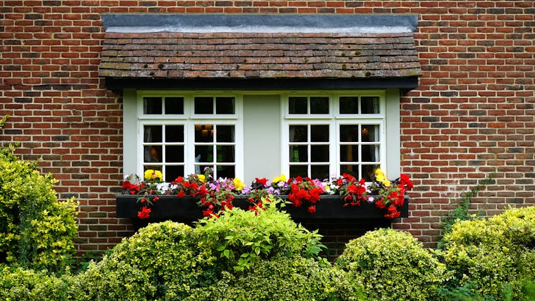 Brick cottage window adorned with vibrant flower box in lush garden setting.