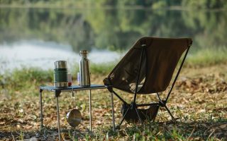 A peaceful lakeside campsite with a folding chair, table, thermoses, and saucepan.