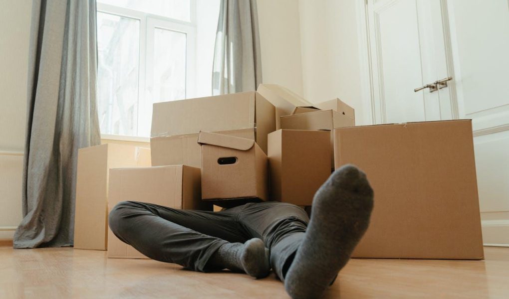 Person in black pants underneath a pile of cardboard boxes