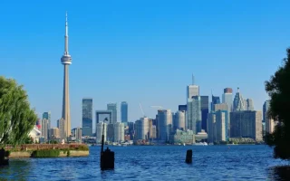 Toronto skyline with the CN Tower and modern skyscrapers viewed across Lake Ontario on a clear sunny day.