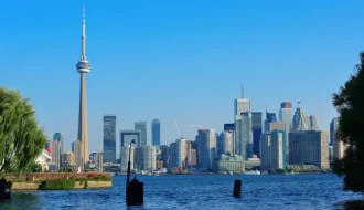 Toronto skyline with the CN Tower and modern skyscrapers viewed across Lake Ontario on a clear sunny day.