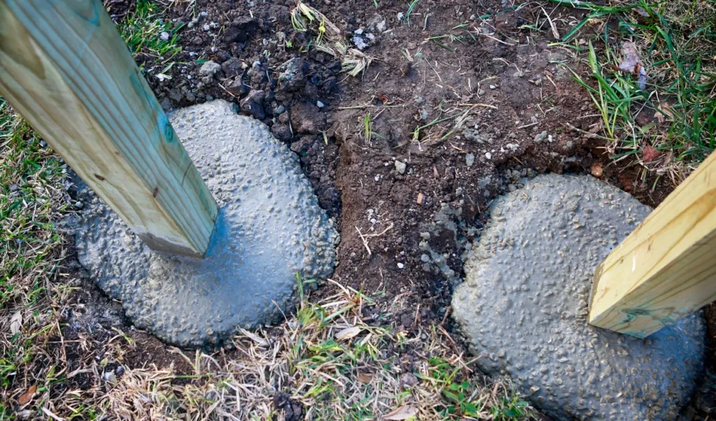 Newly installed pressure-treated wooden fence post secured in a sloped concrete base.